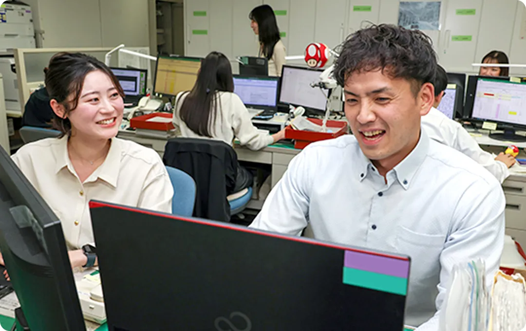 職場でパソコンを見ながら談笑する2人